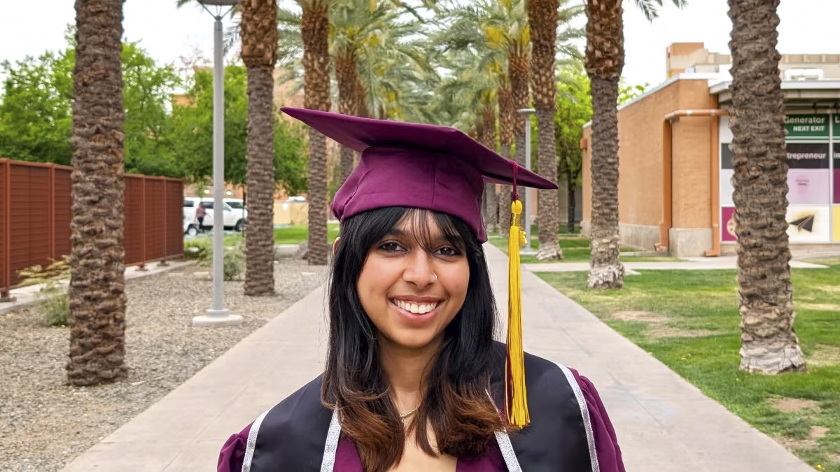 Ana Girish, 2025 spring grad, stands in her cap and gown on palm walk for a portrait shot.